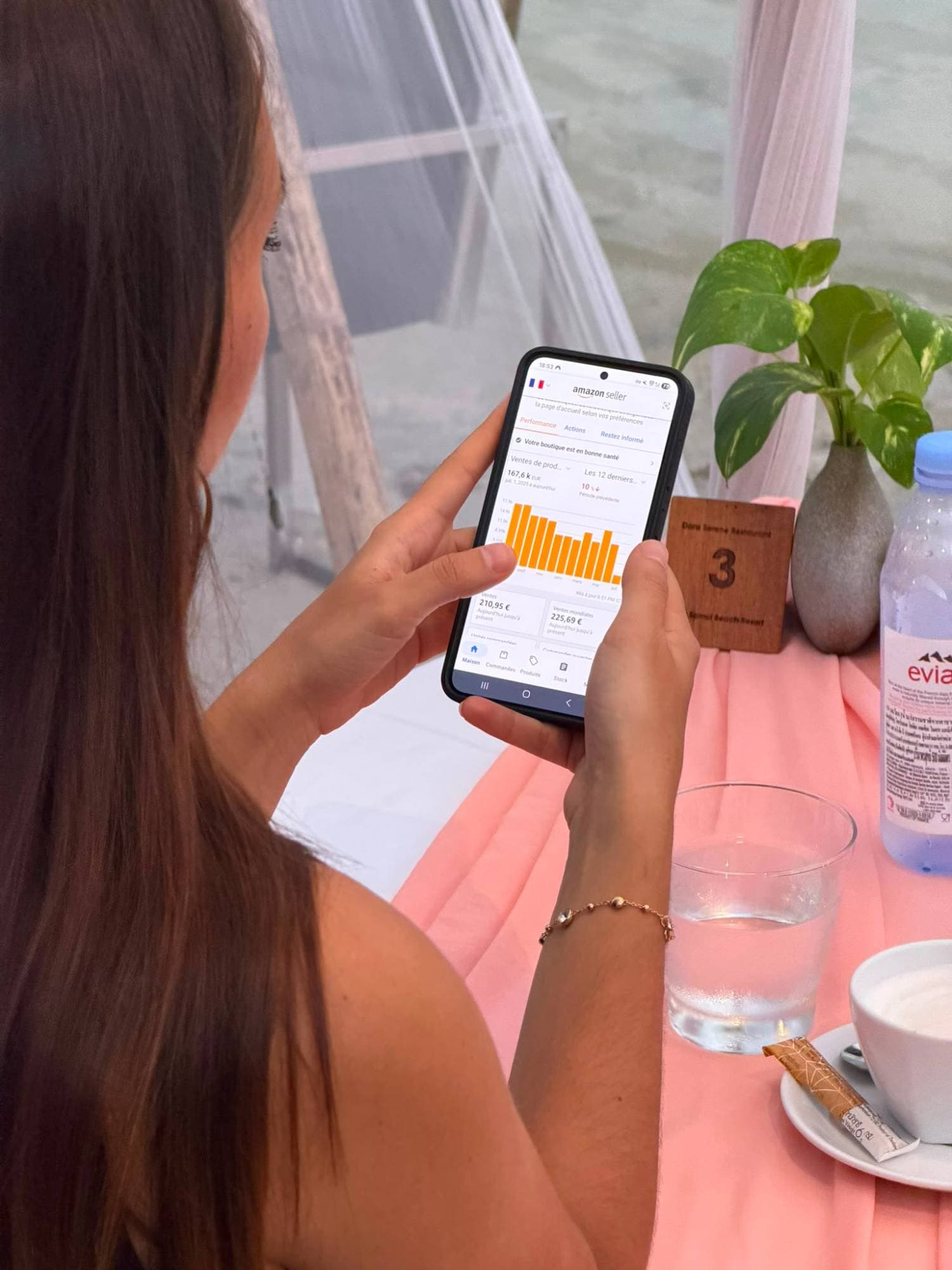 Daphné Saï consulte l'application Amazon Seller de sa marque depuis une table en bord de mer